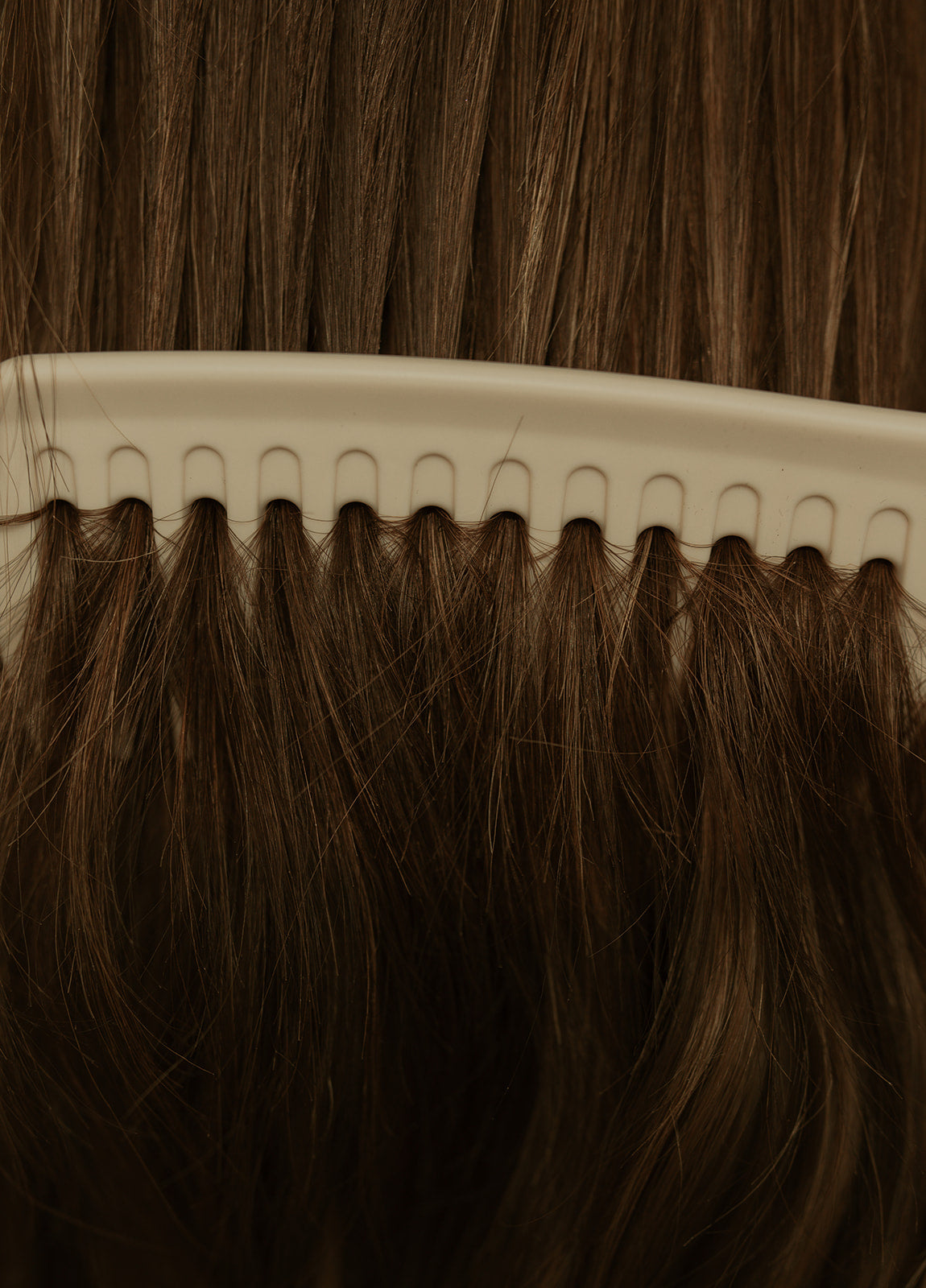 Close-up of a comb going through a  brown balayage virgin hair wig
